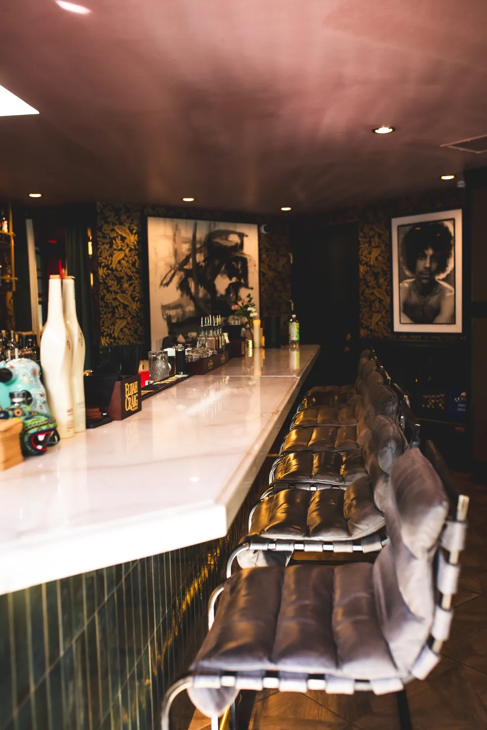 ASA's marble bar with leather stools, gold-patterned wallpaper, and gallery art